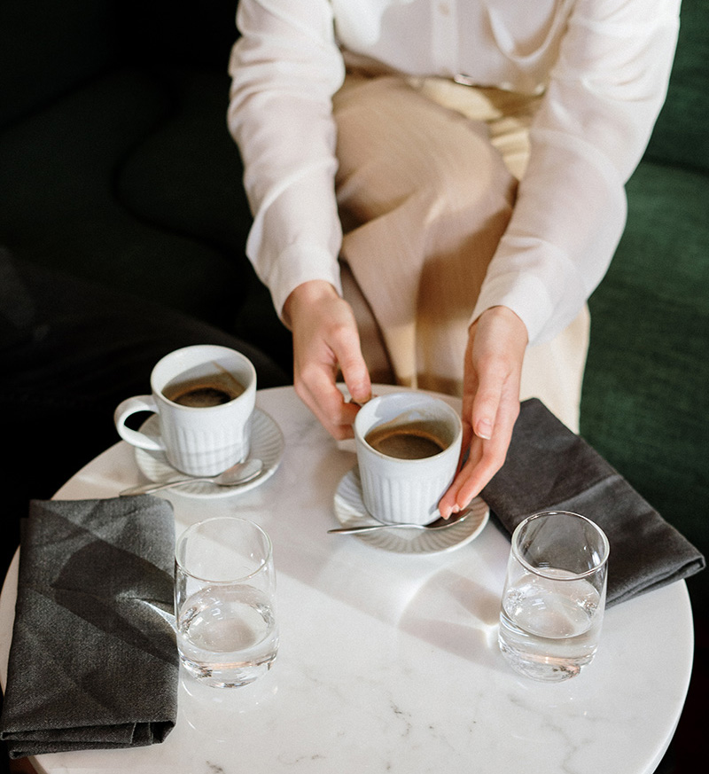 Woman holding white ceramic cup sitting at a table